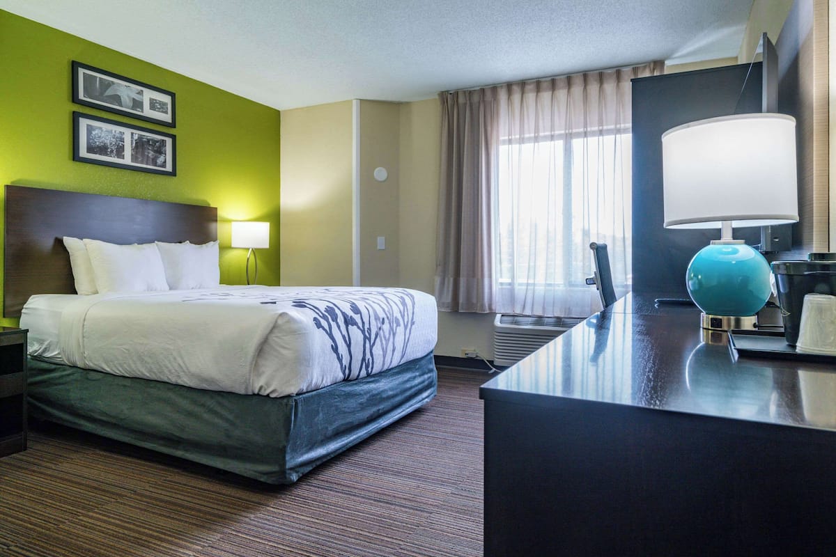 A hotel room with a bed, a desk, a lamp, and a window with curtains.