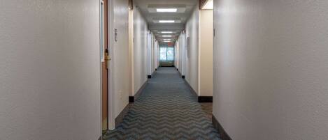 A long, narrow hotel corridor with a patterned carpet, doors on both sides, and a ceiling with recessed lighting.