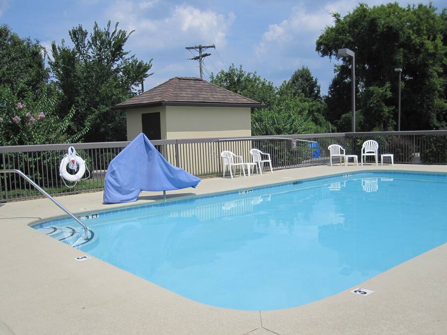 Una piscina rectangular con un flotador de salvamento en la cerca, rodeada de sillas blancas y una zona cubierta.