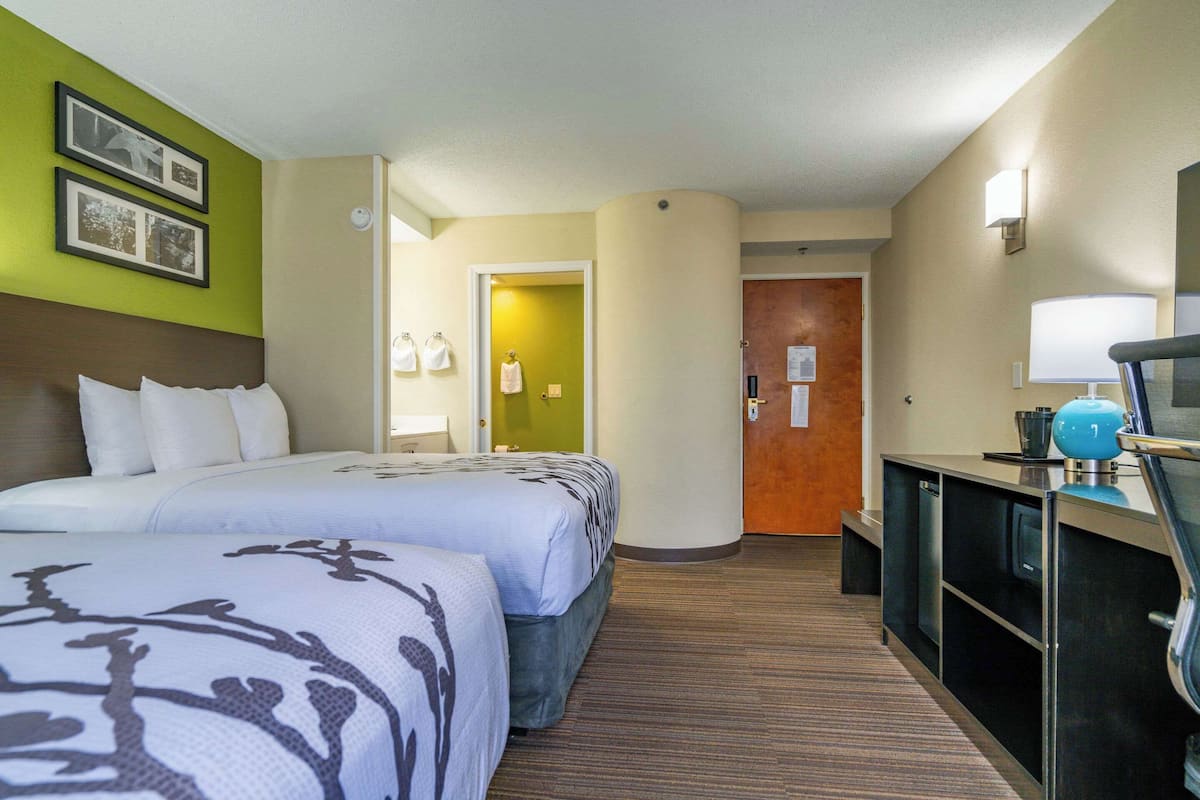 A hotel room with two beds, a desk, a lamp, and a mirror.