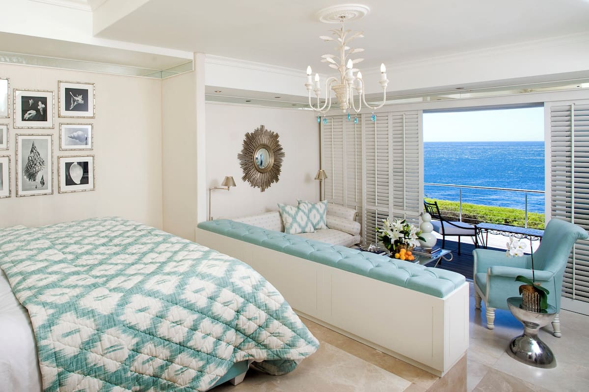 A bedroom with a large bed, a seating area with a view, and a balcony with a table and chairs.