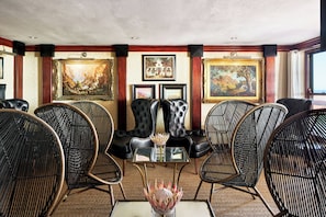 A room with a glass-top table surrounded by wicker chairs, a black leather sofa, and framed artwork on the walls.