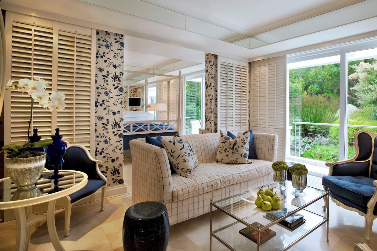 A spacious living room with a sofa, armchairs, a coffee table, and a view of greenery through large windows.