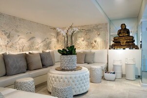 A modern living room with a sofa, ottomans, a Buddha statue, and a decorative wall mural.