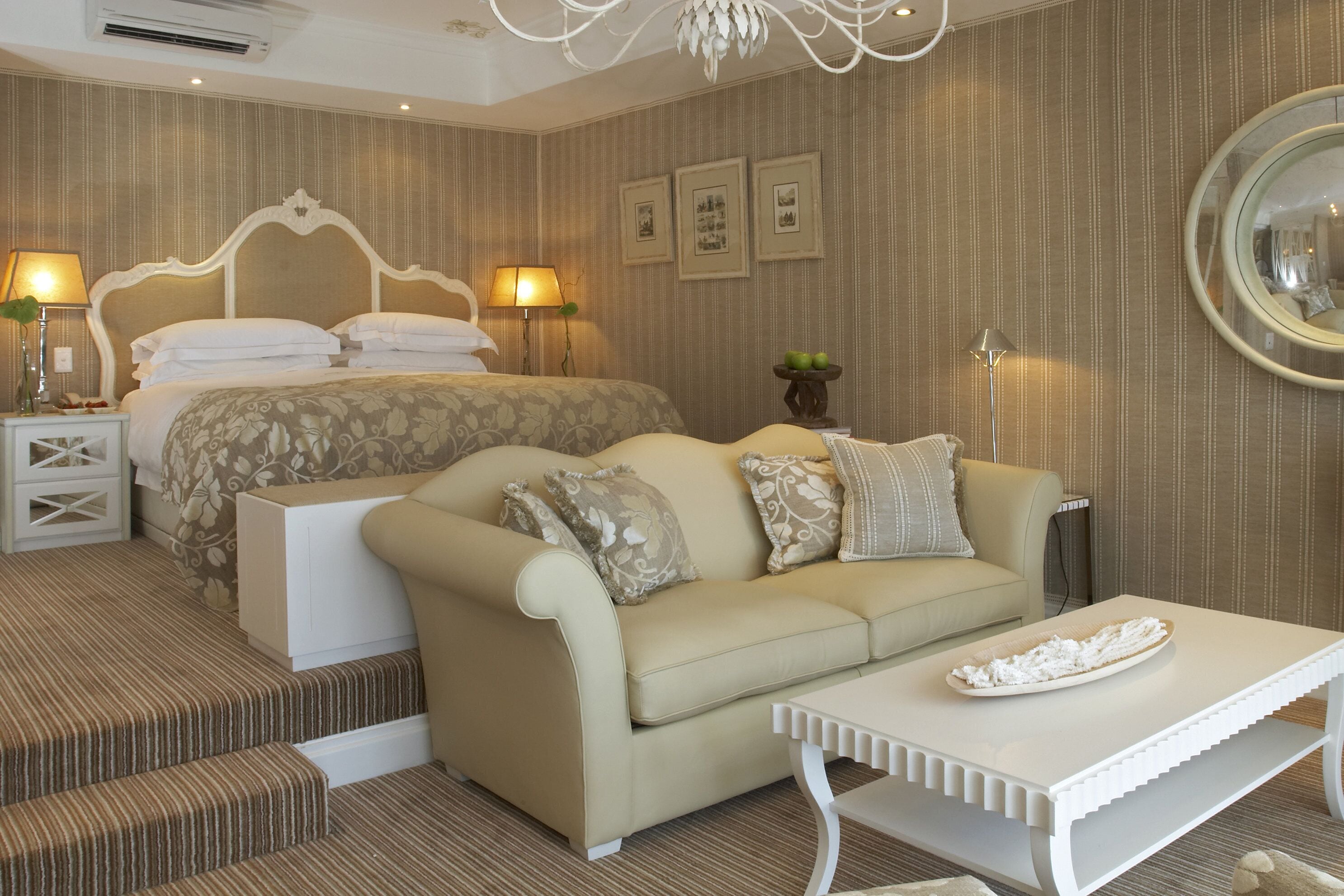 A hotel room with a large bed, a sofa, a coffee table, and a nightstand with lamps.