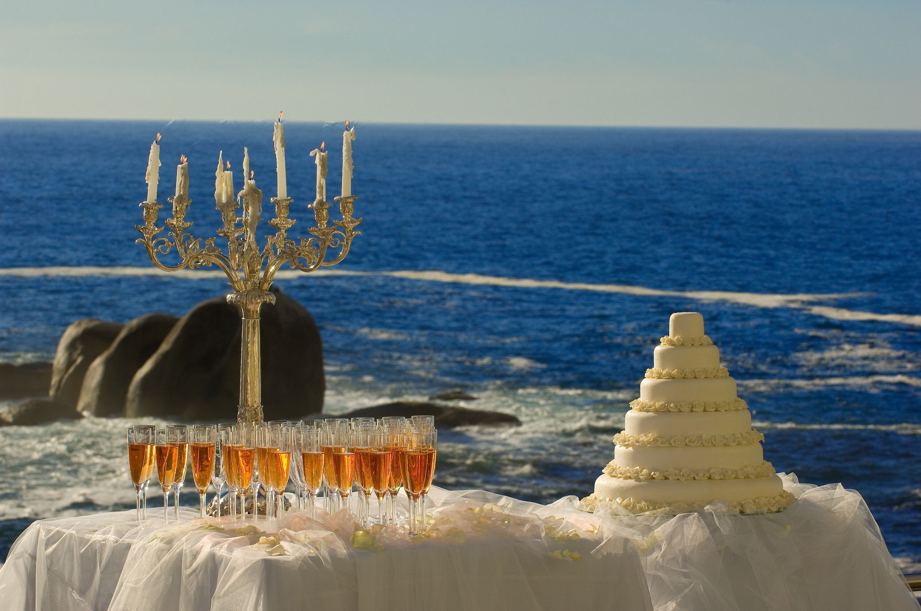 A table with a white tablecloth, a white cake, and glasses of a golden beverage.