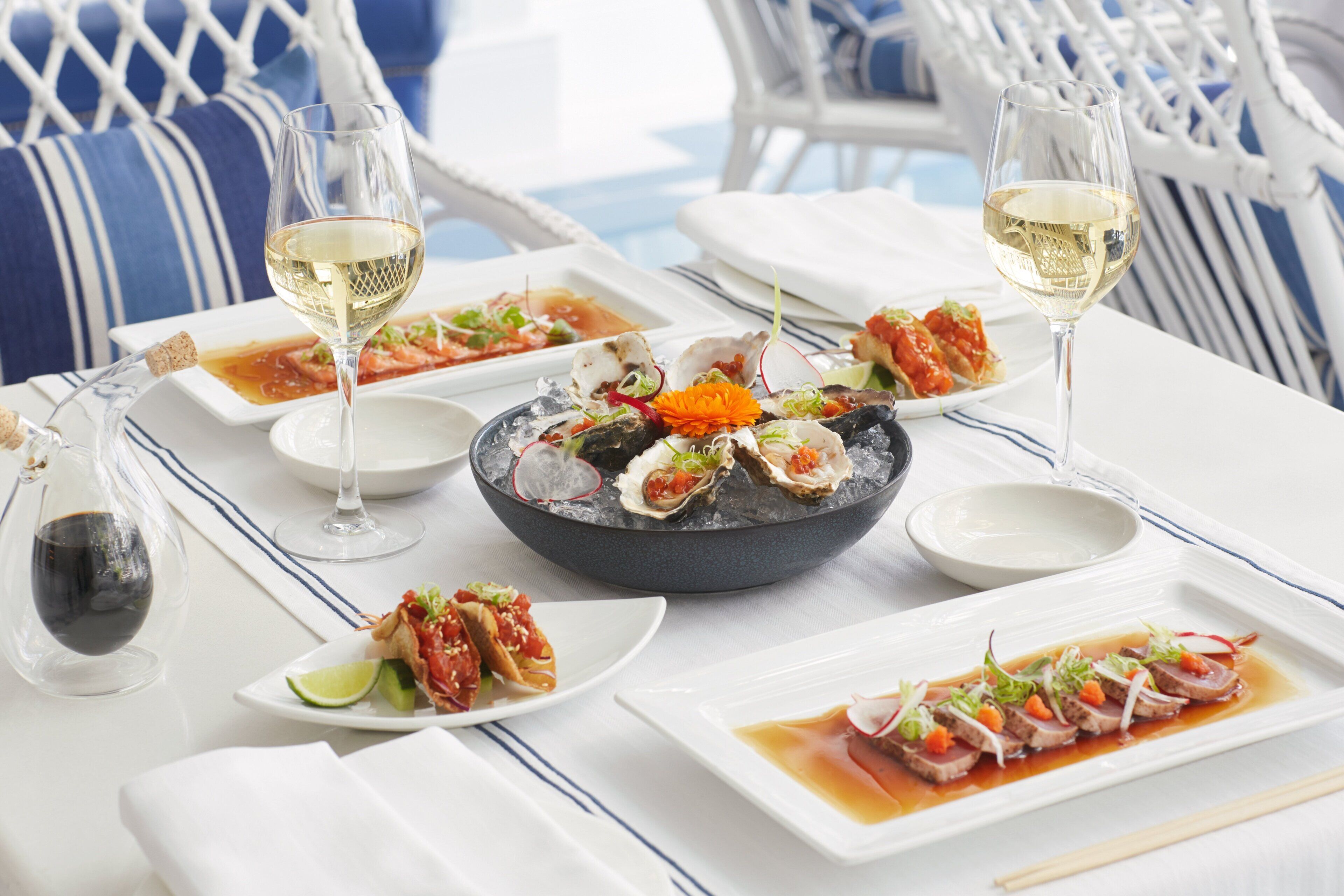Una mesa servida con platos de mariscos, copas de vino y una botella.