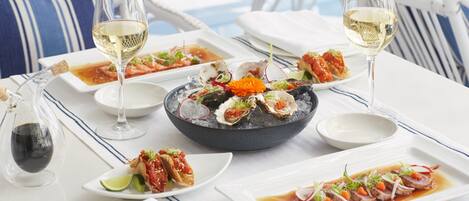 Una mesa servida con platos de mariscos, copas de vino y una botella.