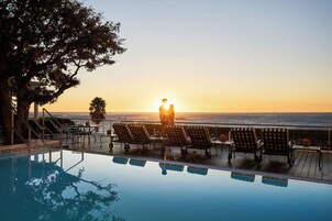 A poolside area with a sunset view, lounge chairs, and a person standing by the pool.