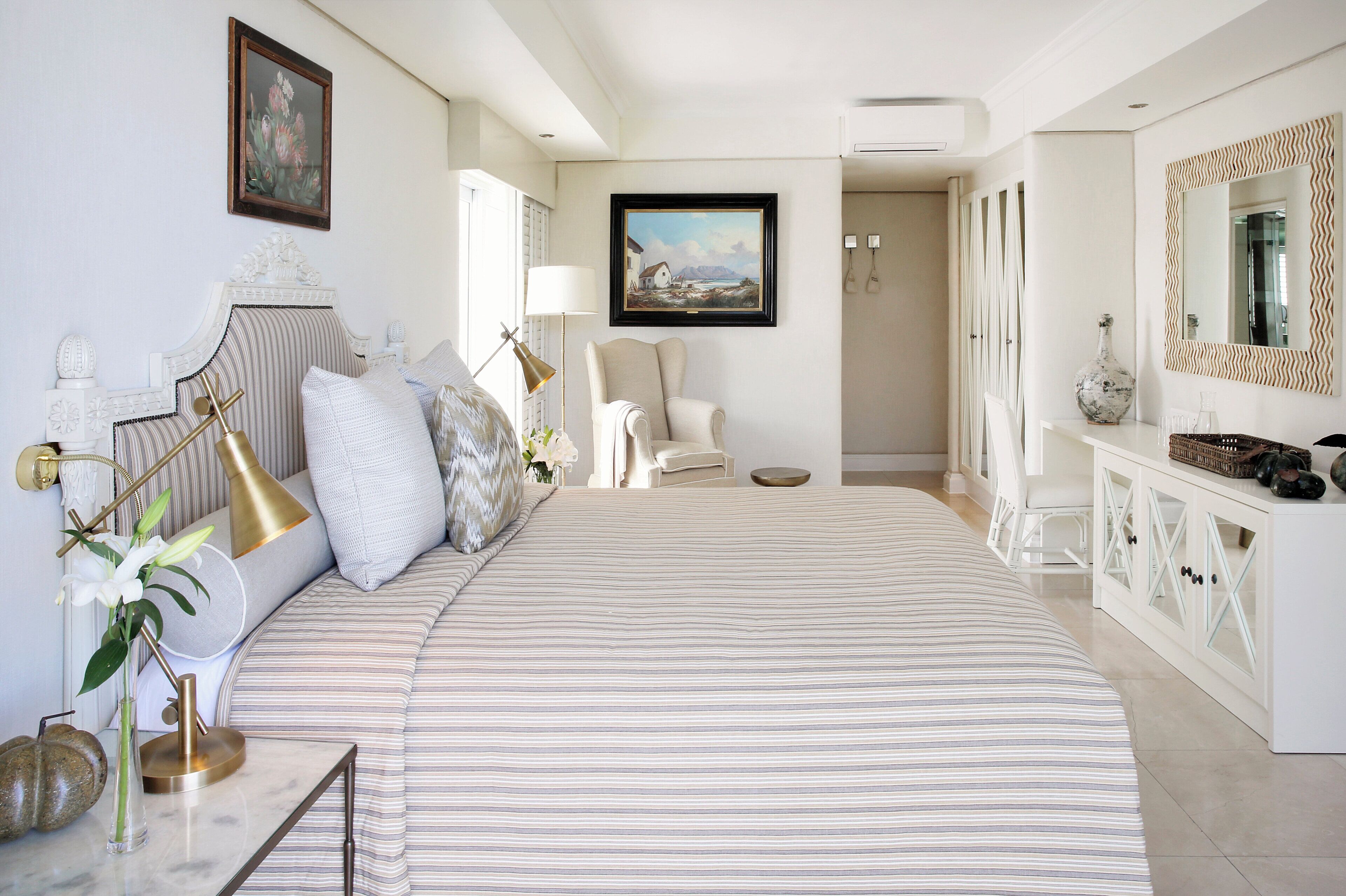 Un dormitorio amplio con una cama grande, una mesita de noche con lámpara, una silla y un aparador con espejo.
