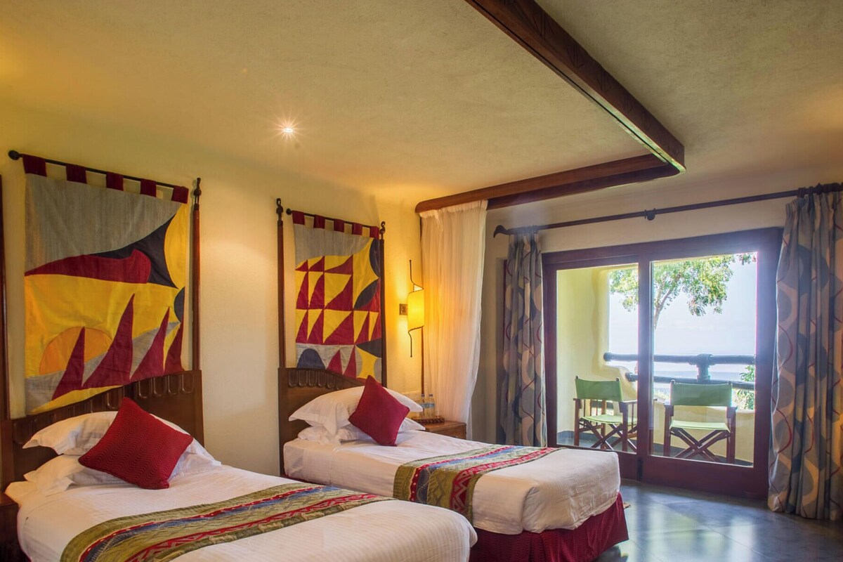 Une chambre d’hôtel avec deux lits, un bureau, une chaise, une lampe et une vue sur l’extérieur.