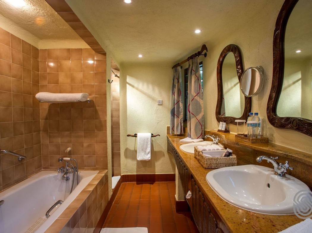 Een badkamer met een bad, twee wastafels, een wastafelmeubel en een grote spiegel.
