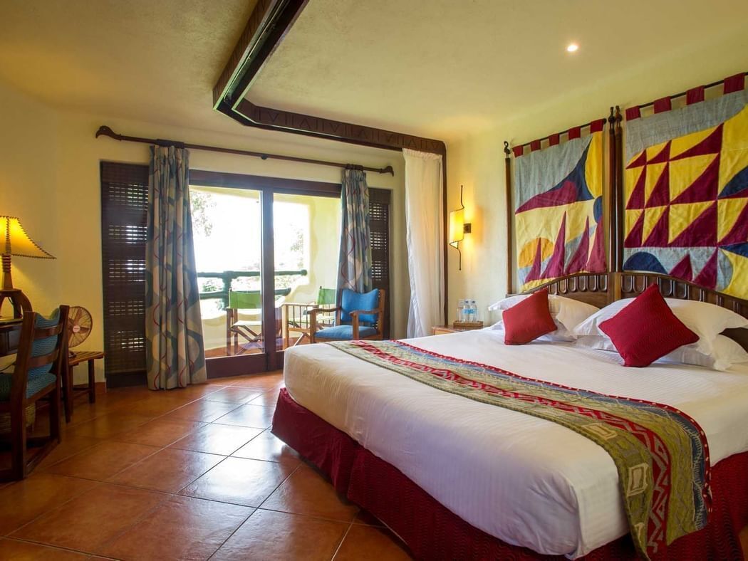 Une chambre d’hôtel avec un grand lit, un coin repas avec des chaises et une vue sur l’extérieur, accessible par une porte coulissante.