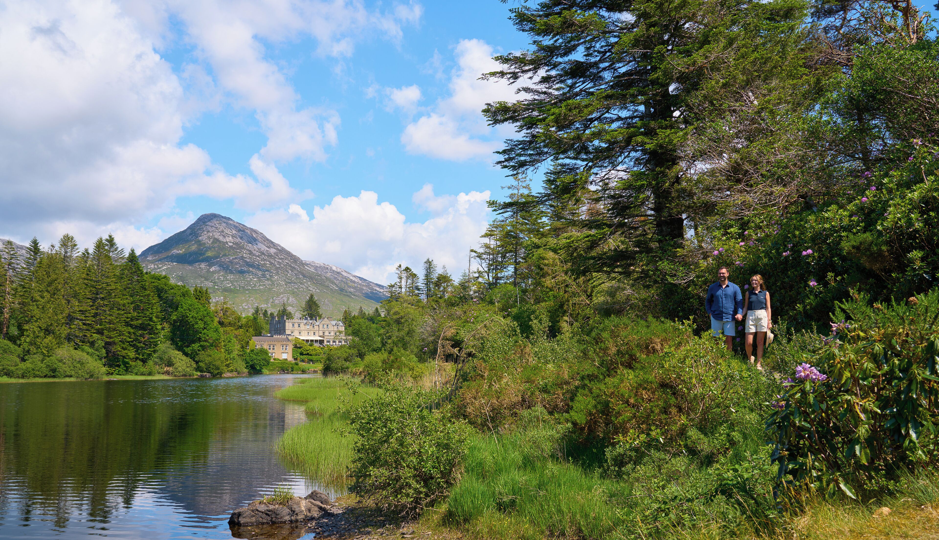 A scenic view of a lake with a mountain in the background, surrounded by lush greenery and a building with a traditional architectural style.