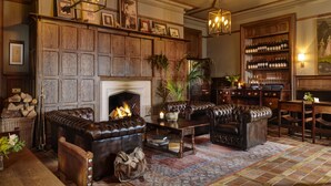 A traditional library with leather sofas, a fireplace, bookshelves, and a wine rack. - Ballynahinch Castle Hotel (Ballynahinch)