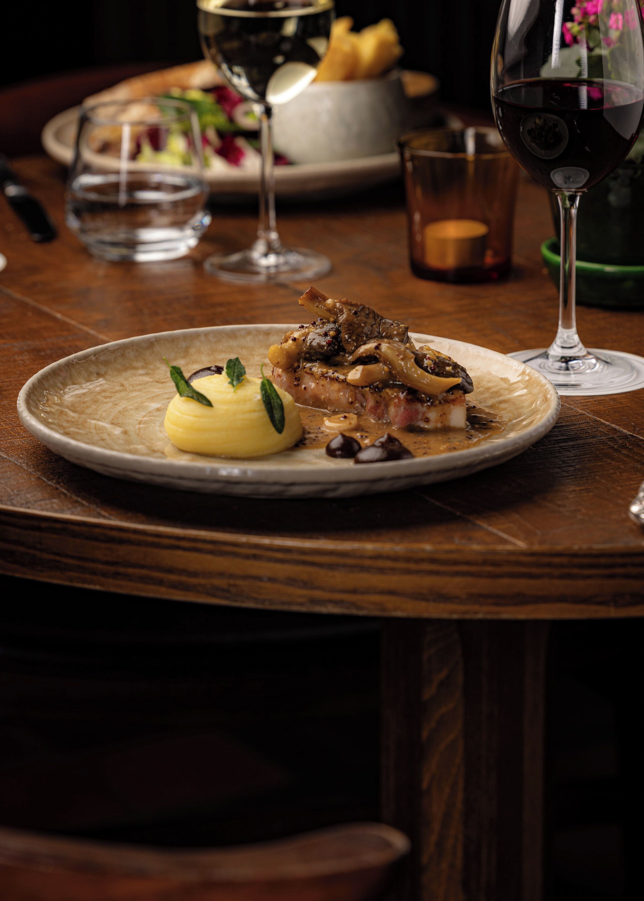 A dining table with a plate of food, a glass of red wine, and a candle.