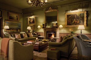 A traditional room with a fireplace, green upholstered furniture, and framed artwork on the walls. - Ballynahinch Castle Hotel (Ballynahinch)