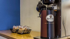 A coffee machine branded 'Royal Cup Coffee' with a 'Bunn' logo, a basket of bread, and a bag of sugar on a wooden counter. - Rodeway Inn Charlotte (Charlotte)