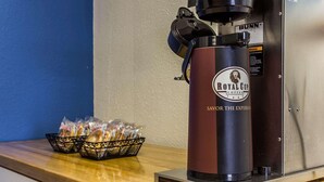 A coffee machine branded 'Royal Cup Coffee' with a 'Bunn' logo, a basket of bread, and a bag of sugar on a wooden counter.