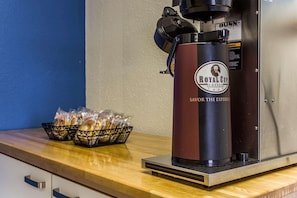 A coffee machine branded 'Royal Cup Coffee' with a 'Bunn' logo, a basket of bread, and a bag of sugar on a wooden counter. - Rodeway Inn Charlotte (Charlotte)