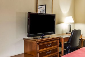 A hotel room with a wooden desk, a television, a lamp, and a chair. - Rodeway Inn Charlotte (Charlotte)
