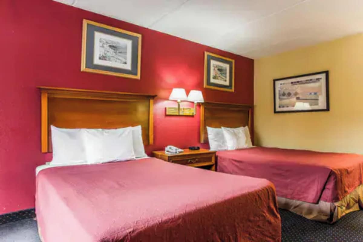 A hotel room with two beds, each with a wooden headboard, a nightstand with a lamp, and framed pictures on the walls.