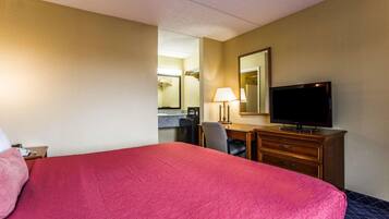 Quarto de hotel com uma cama grande, uma escrivaninha com cadeira, televisão e espelho.