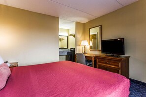 A hotel room with a large bed, a desk with a chair, a television, and a mirror. - Rodeway Inn Charlotte (Charlotte)