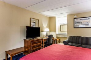 A hotel room with a bed, a desk with a television, a chair, a sofa, and a mirror on the wall. - Rodeway Inn Charlotte (Charlotte)