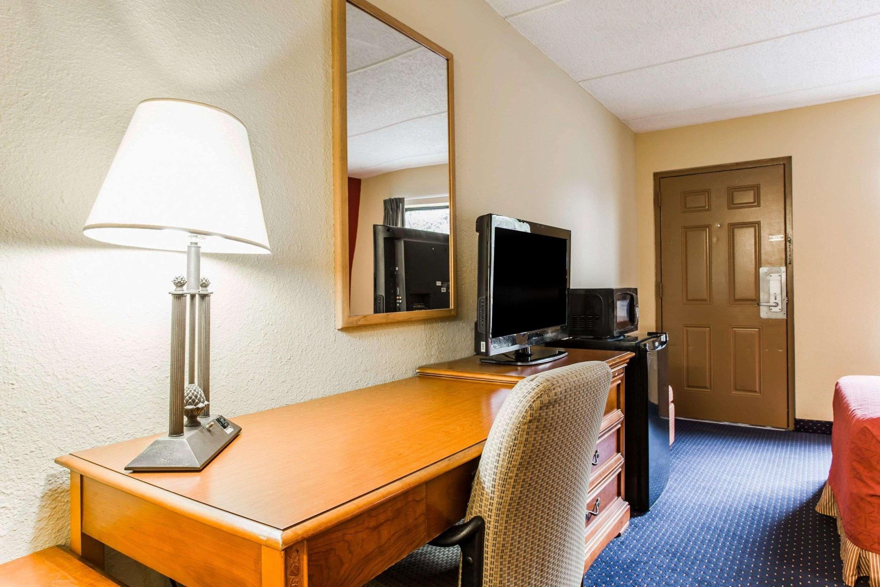 Een hotelkamer met een houten bureau, een televisie, een lamp, een spiegel, een dressoir en een deur.