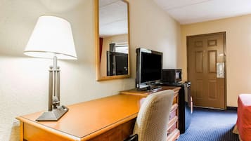 Een hotelkamer met een houten bureau, een televisie, een lamp, een spiegel, een dressoir en een deur.