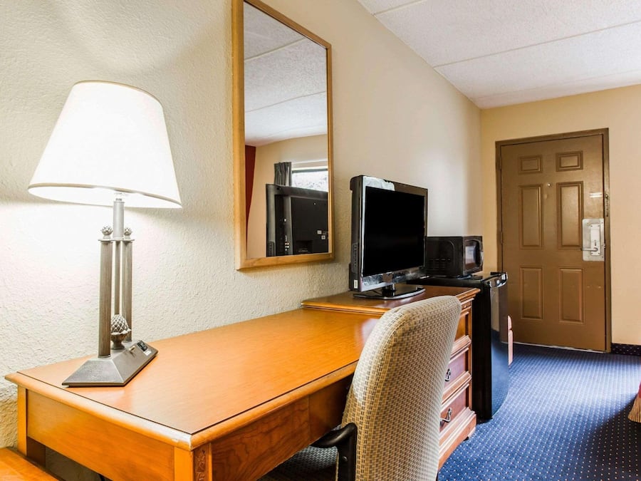Een hotelkamer met een houten bureau, een televisie, een lamp, een spiegel, een dressoir en een deur.