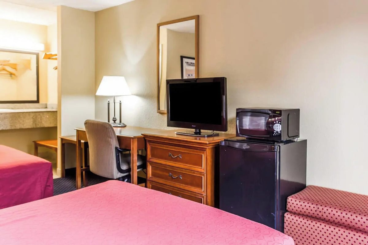 A hotel room with a bed, a desk with a computer, a television, a microwave, and a dresser.