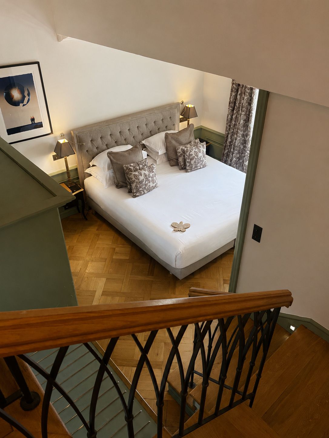 A bedroom with a large bed, two bedside tables, a headboard, and a staircase.