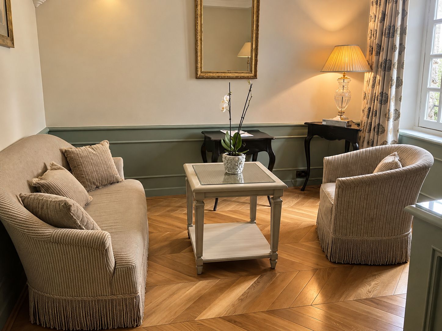 Een woonkamer met een bank, twee fauteuils, een bijzettafeltje, een spiegel en een lamp.