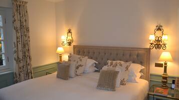 A neatly made bed with multiple pillows, a bedside table with a lamp, and a wall-mounted light fixture.