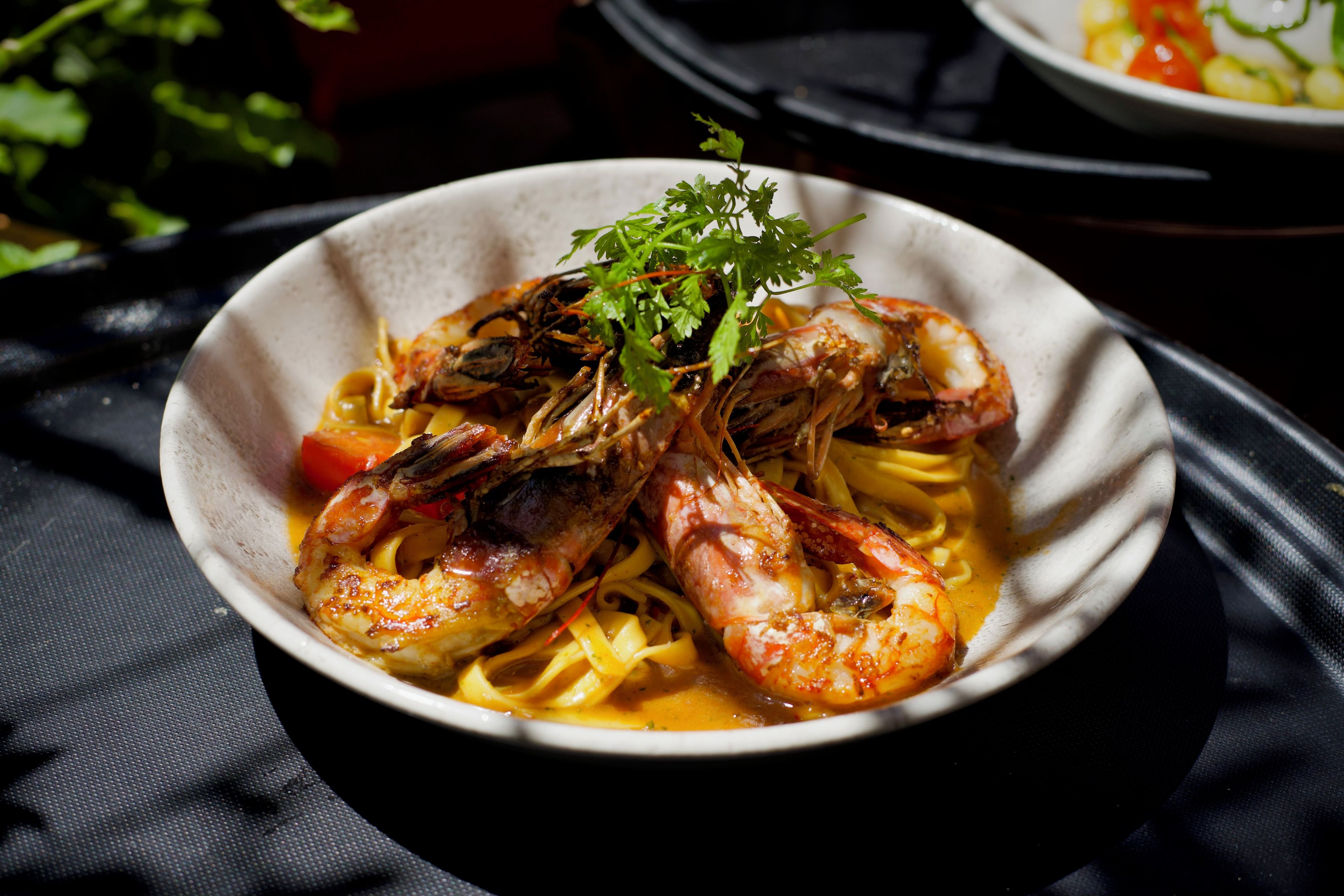 A bowl of pasta with shrimp and vegetables, garnished with parsley.