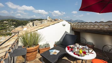 Um terraço com uma mesa posta para dois, plantas em vasos e vista para uma cidade e montanhas.