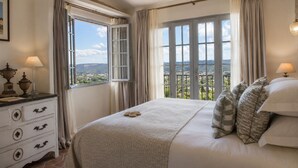 A bedroom with a large bed, two windows with curtains, a dresser with lamps, and a view of the countryside. - Le Saint Paul (Saint-Paul-de-Vence)