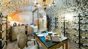A dining area with a stone wall, a chandelier, and wine bottles on shelves. - Le Saint Paul (Saint-Paul-de-Vence)