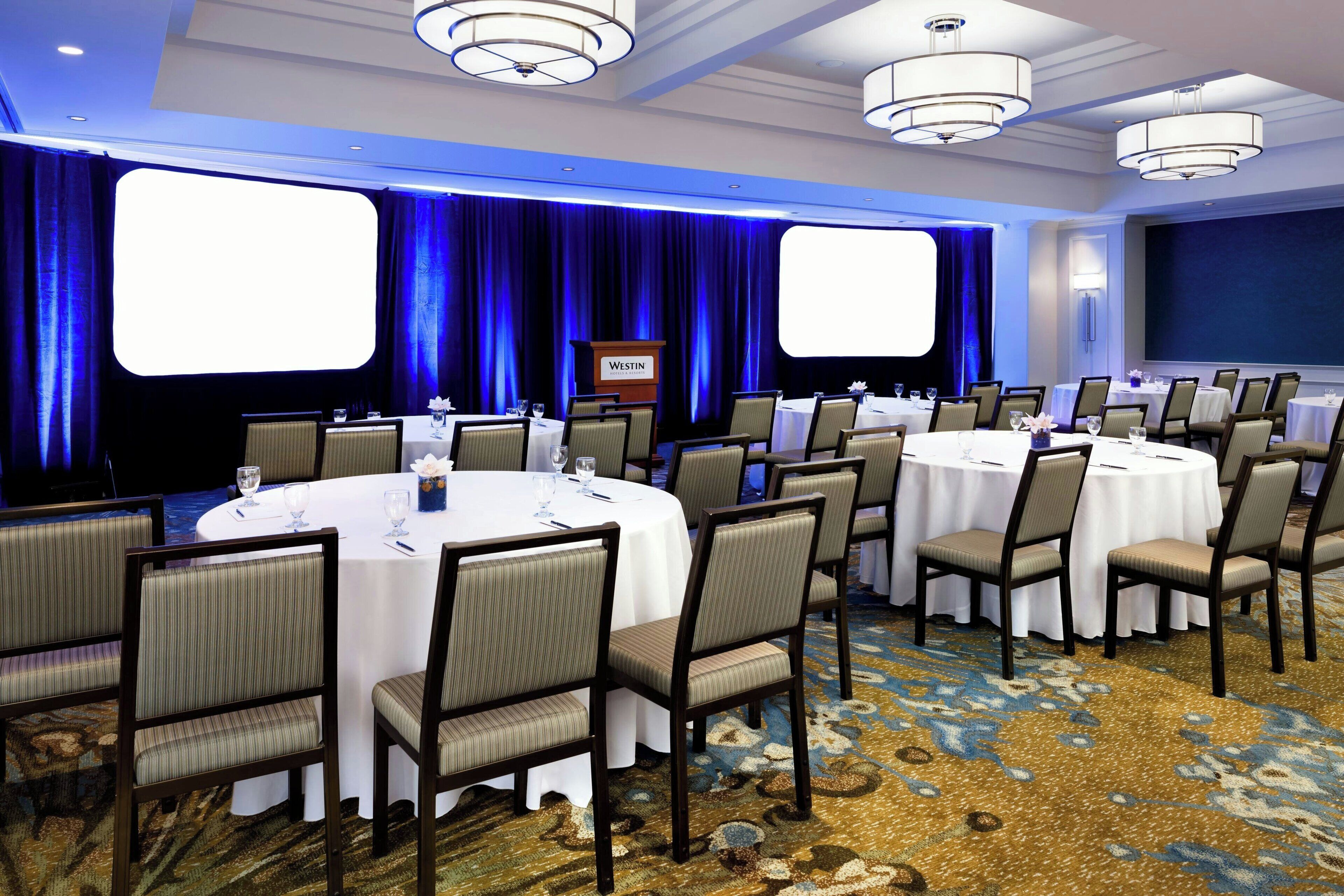 A conference room with round tables, chairs, and a stage with a podium.
