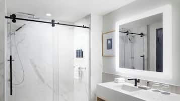 A modern bathroom with a glass-enclosed shower, a large mirror, and a white vanity with a sink.