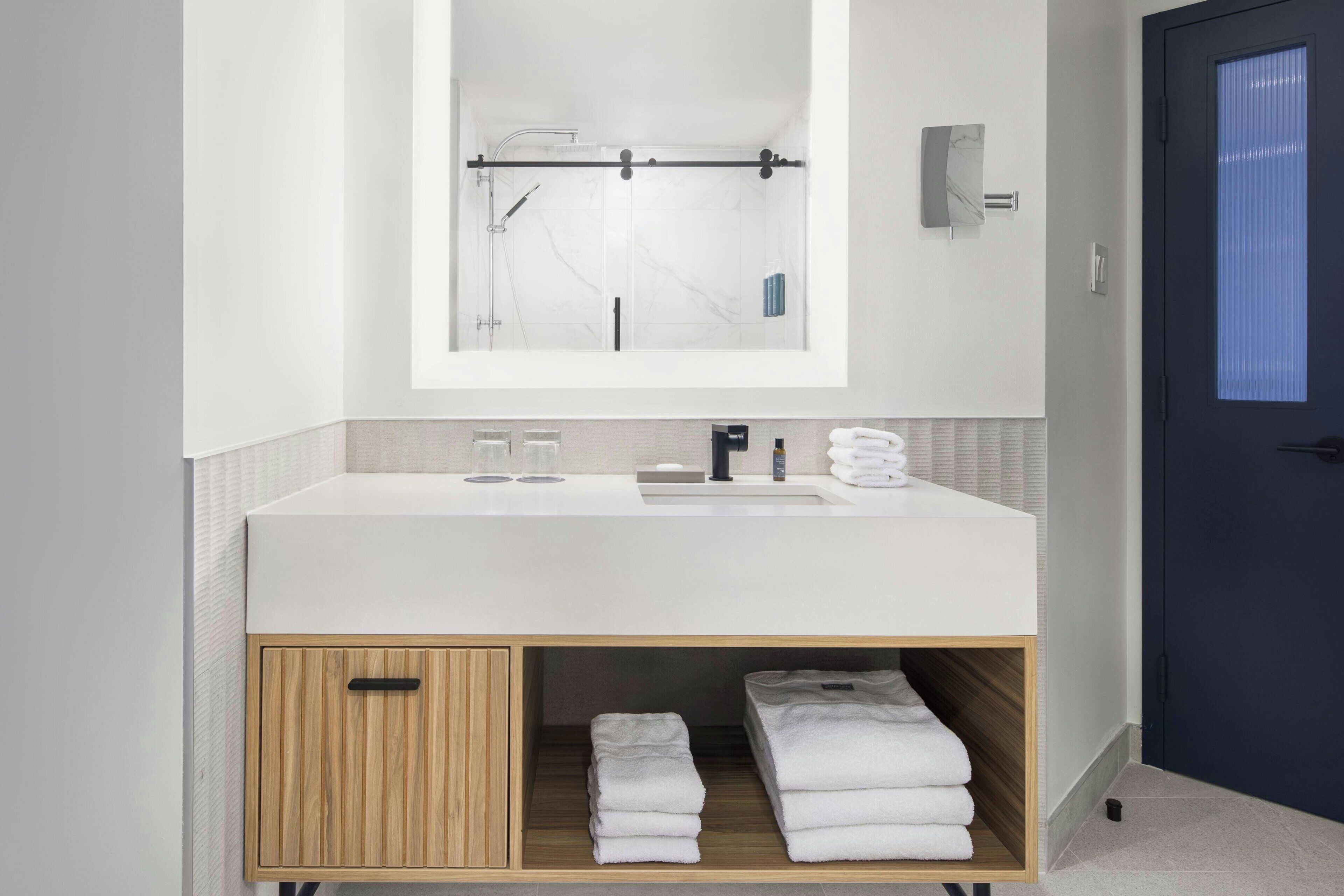 A modern bathroom with a white sink, mirror, and towel storage.
