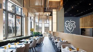 A modern cafe with a long counter, tables, and chairs, large windows, and a distinctive wall art piece. - Le Westin Tremblant (Mont-Tremblant)