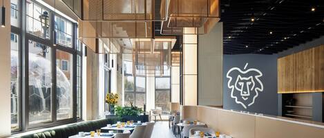 A modern cafe with a long counter, tables, and chairs, large windows, and a distinctive wall art piece.