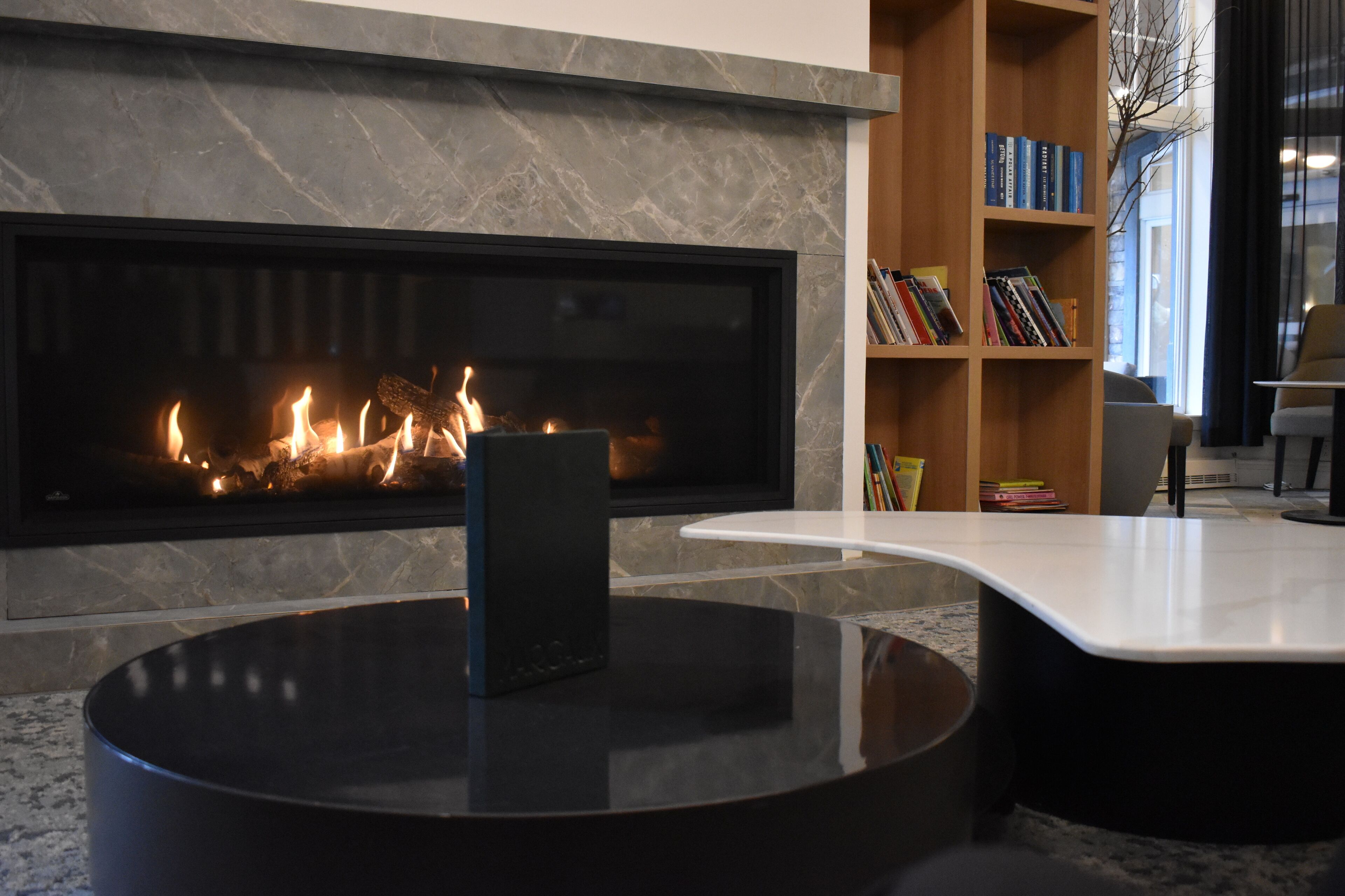 Ein modernes Wohnzimmer mit Kamin, einem runden schwarzen Couchtisch und einer Bücherwand voller Bücher.