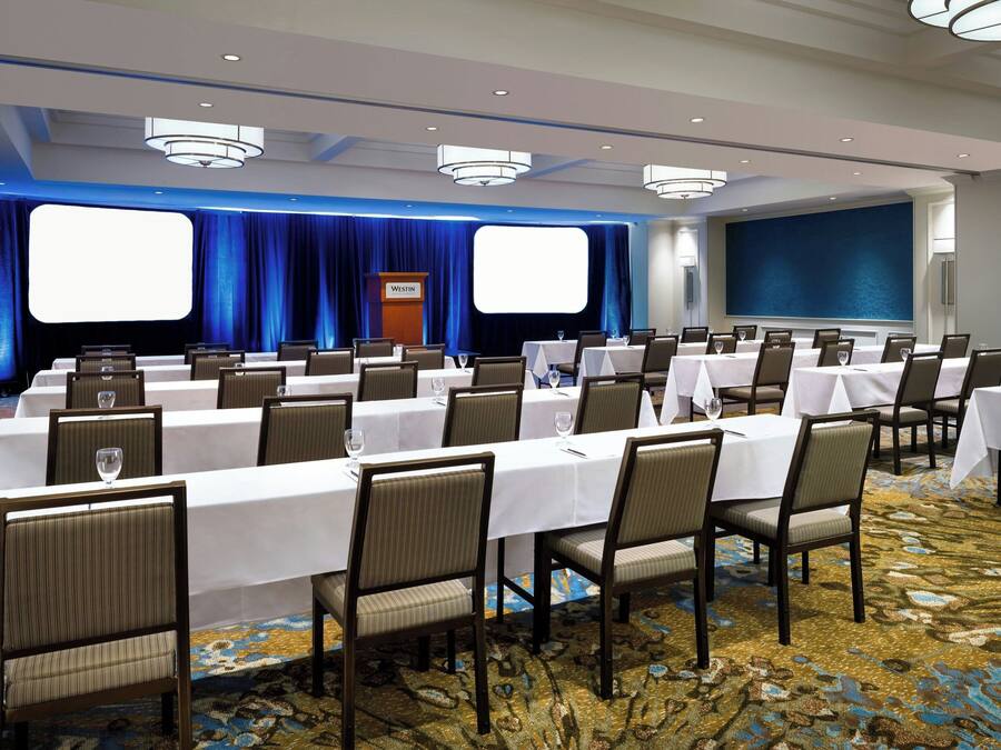 A conference room with multiple tables and chairs, a podium, and a large screen.