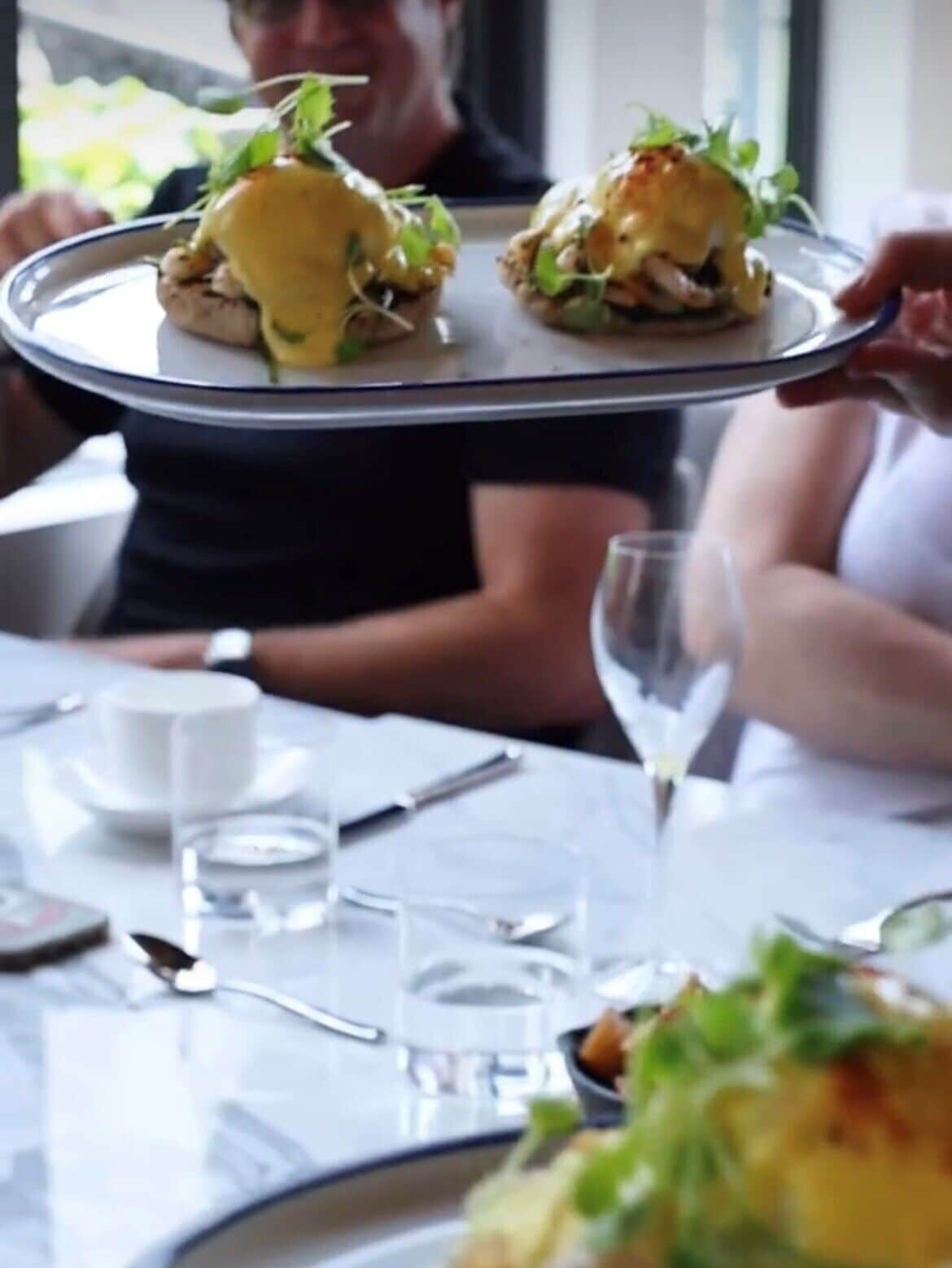 A person holding a tray with two dishes, likely a meal, in a dining setting.