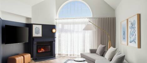 Una sala de estar moderna con chimenea, televisor de pantalla plana, sofá y un ventanal grande.