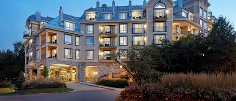 A multi-story hotel with a stone facade, multiple balconies, and a landscaped garden.